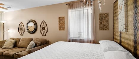 Een slaapkamer met een groot bed, een bank, decoratieve wandkunst en een kroonluchter.