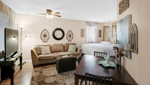 A cozy living room with a sofa, a coffee table, a dining table with chairs, a TV, and a ceiling fan.