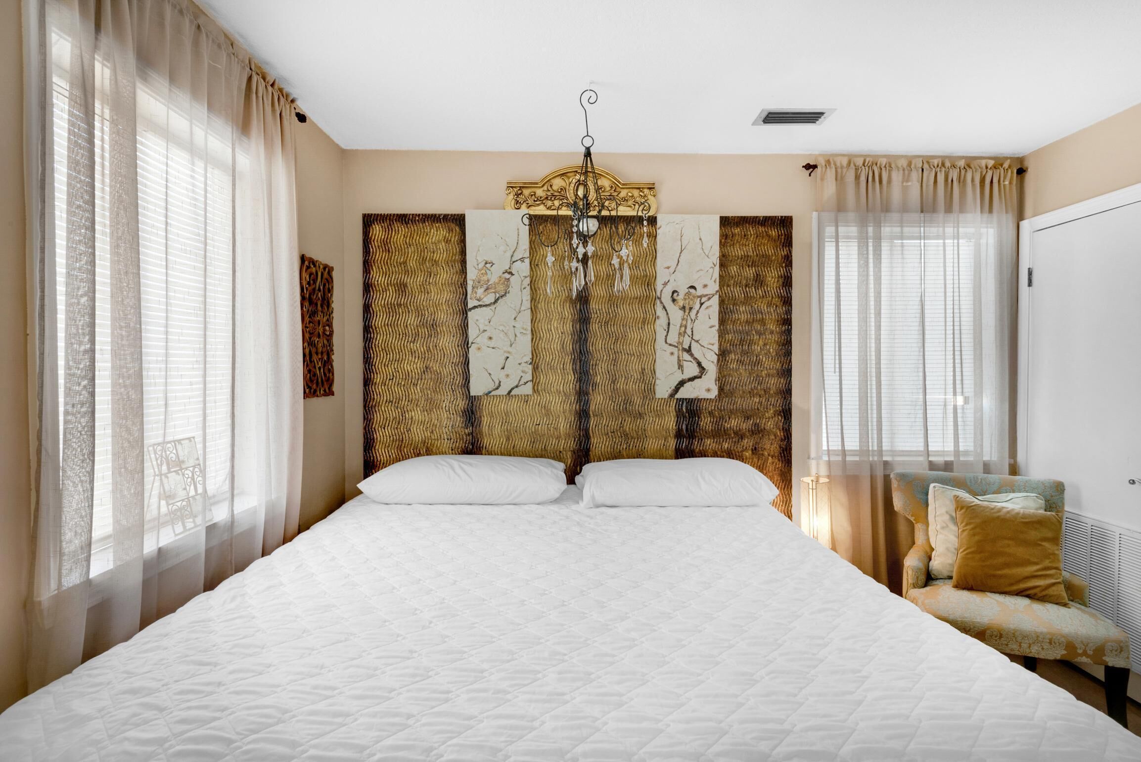 A bedroom with a large bed, a chair, and curtains.