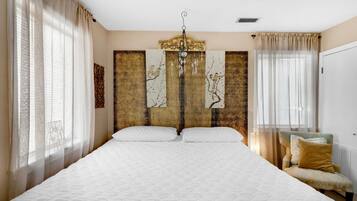A bedroom with a large bed, a chair, and curtains.