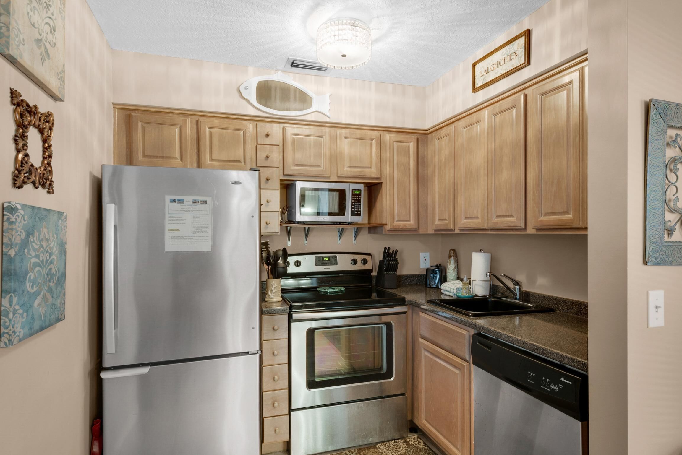 A compact kitchen with stainless steel appliances, wooden cabinets, and a microwave.