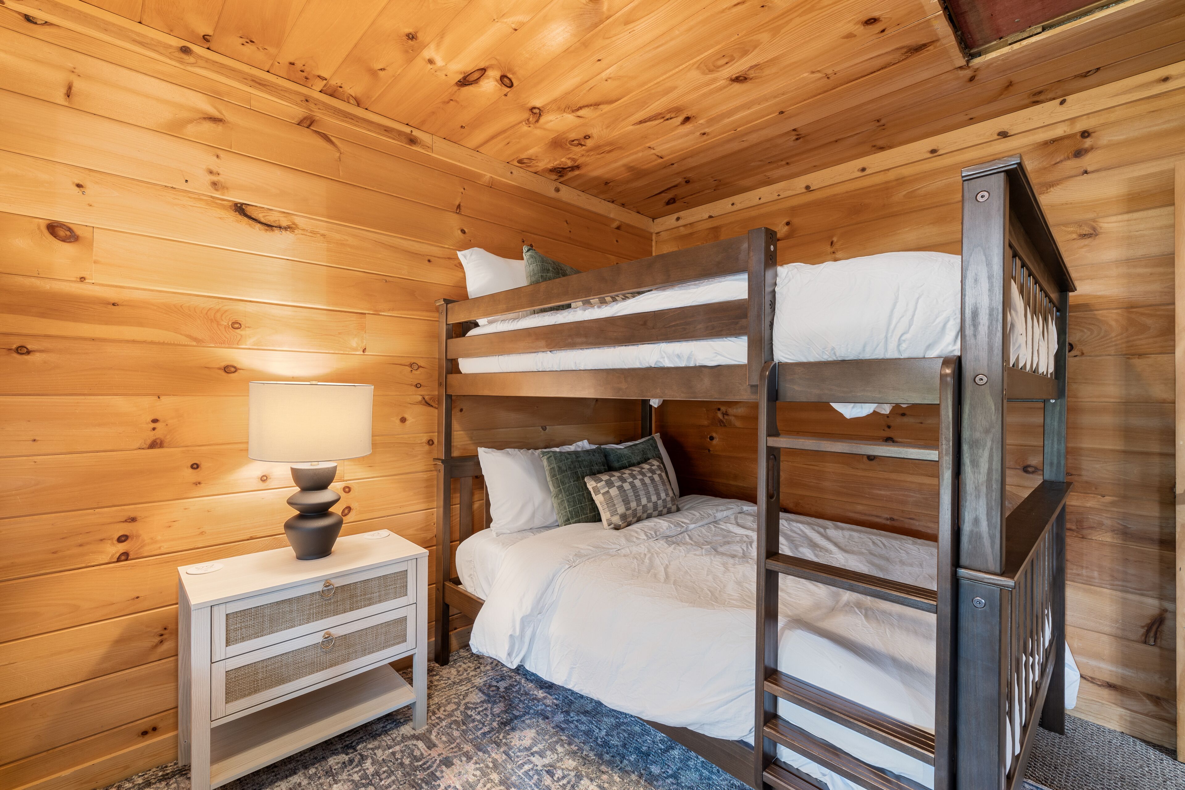 A bunk bed with white bedding and a nightstand with a lamp.