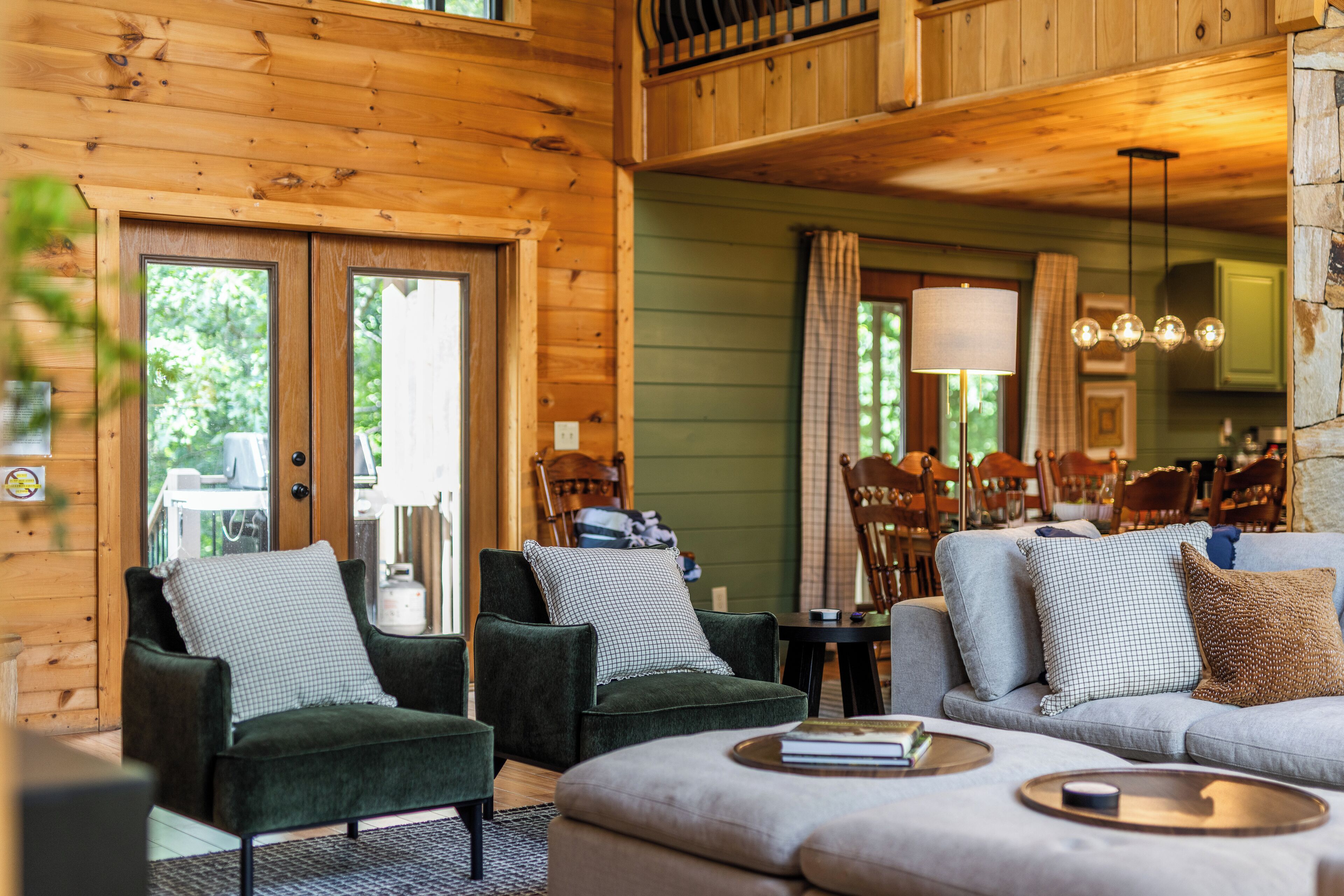 A cozy living room with wooden walls, a sofa, two armchairs, and a dining area with chairs and a table.