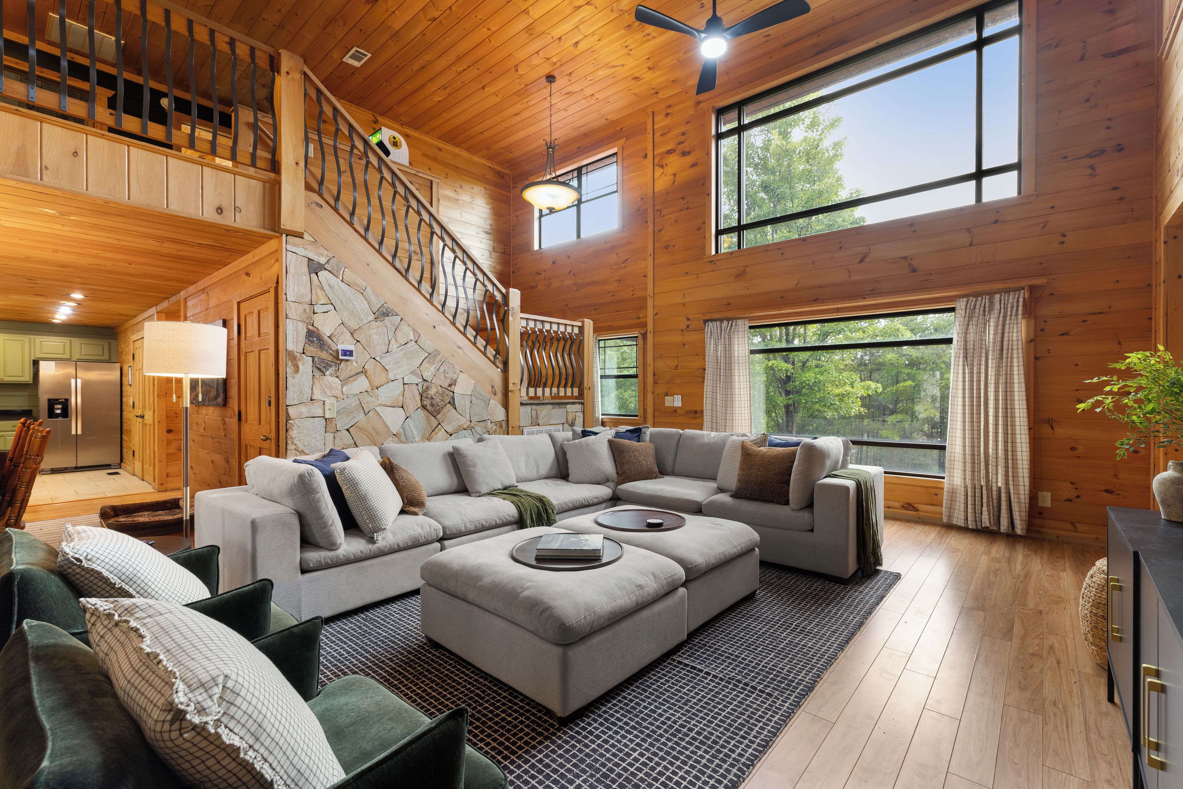 A spacious living room with a large sectional sofa, a staircase, and large windows offering a view of the outdoors.