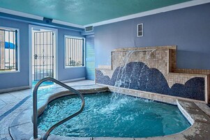 A swimming pool with a water feature, a tiled wall with a mountain design, and a door with a metal gate.