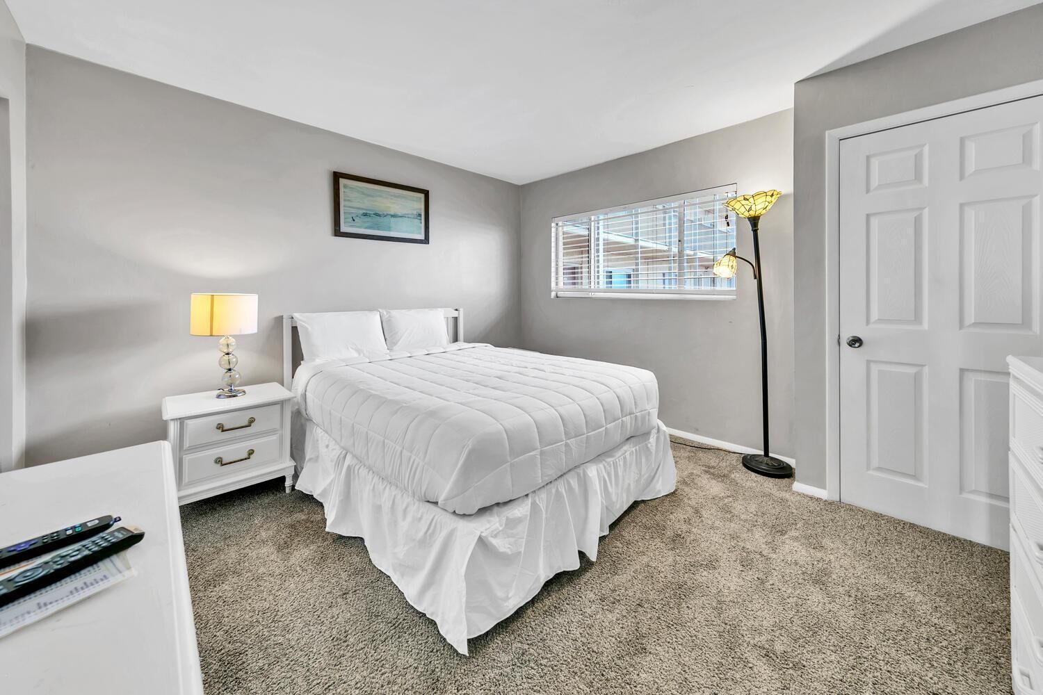 A bedroom with a bed, nightstand, lamp, and a window with blinds.
