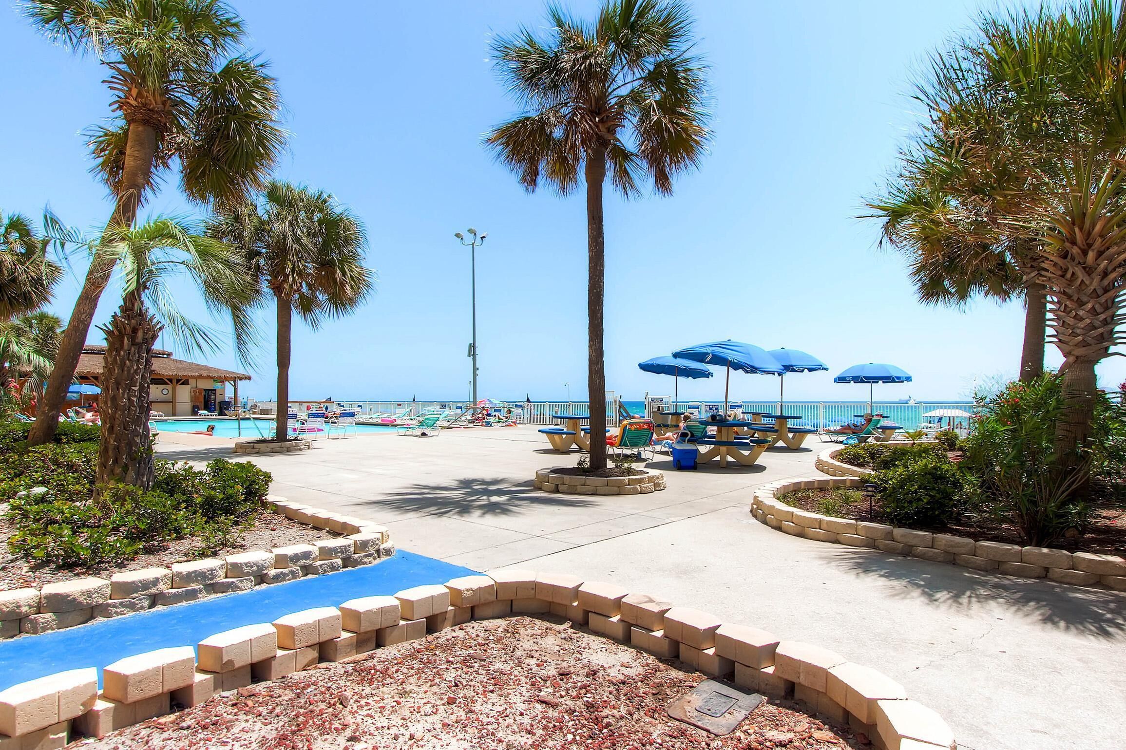 A pool area with palm trees, lounge chairs, and umbrellas.