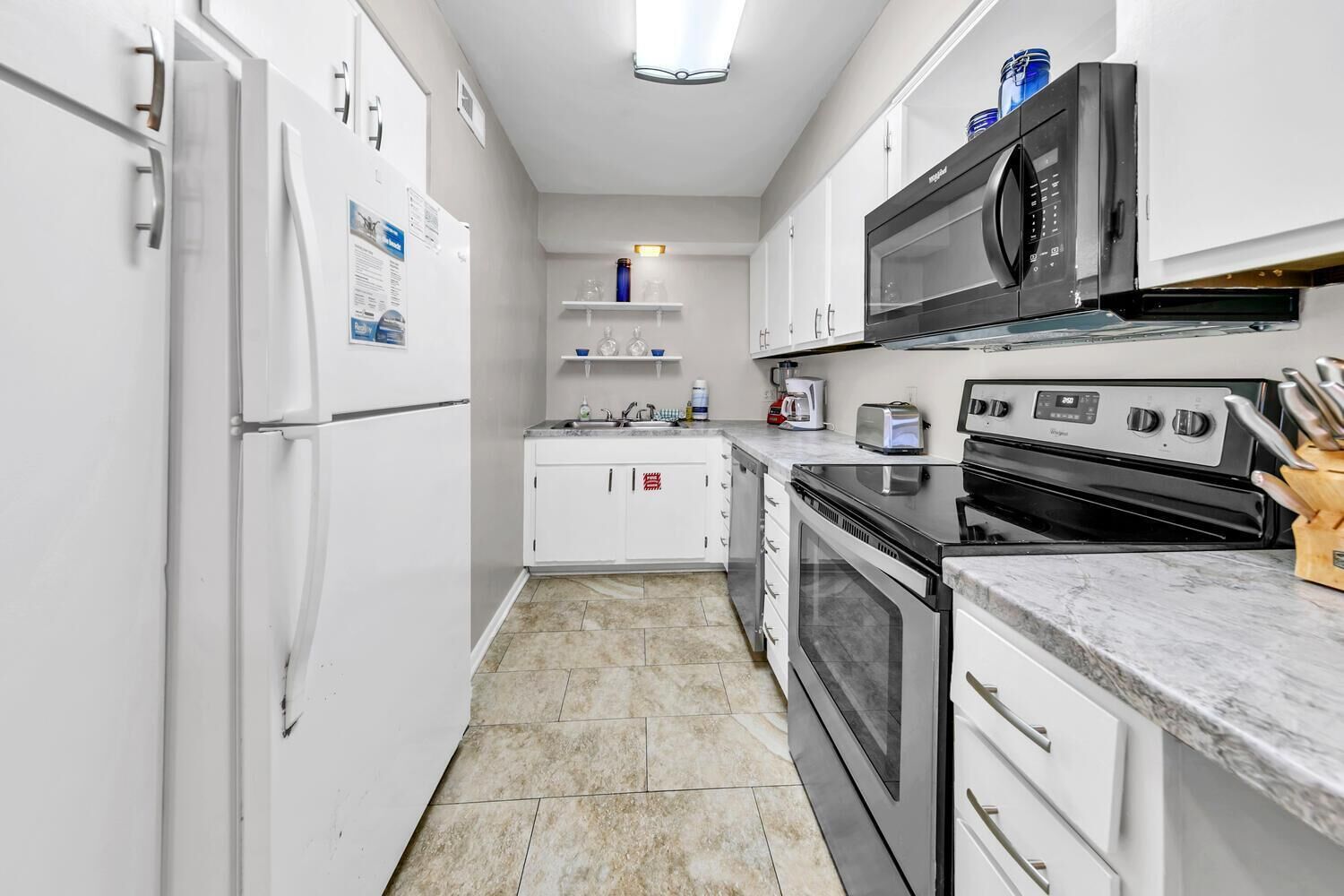 A modern kitchen with white cabinets, a built-in oven, a microwave, and a stainless steel refrigerator.