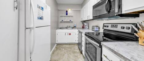 A modern kitchen with white cabinets, a built-in oven, a microwave, and a stainless steel refrigerator.