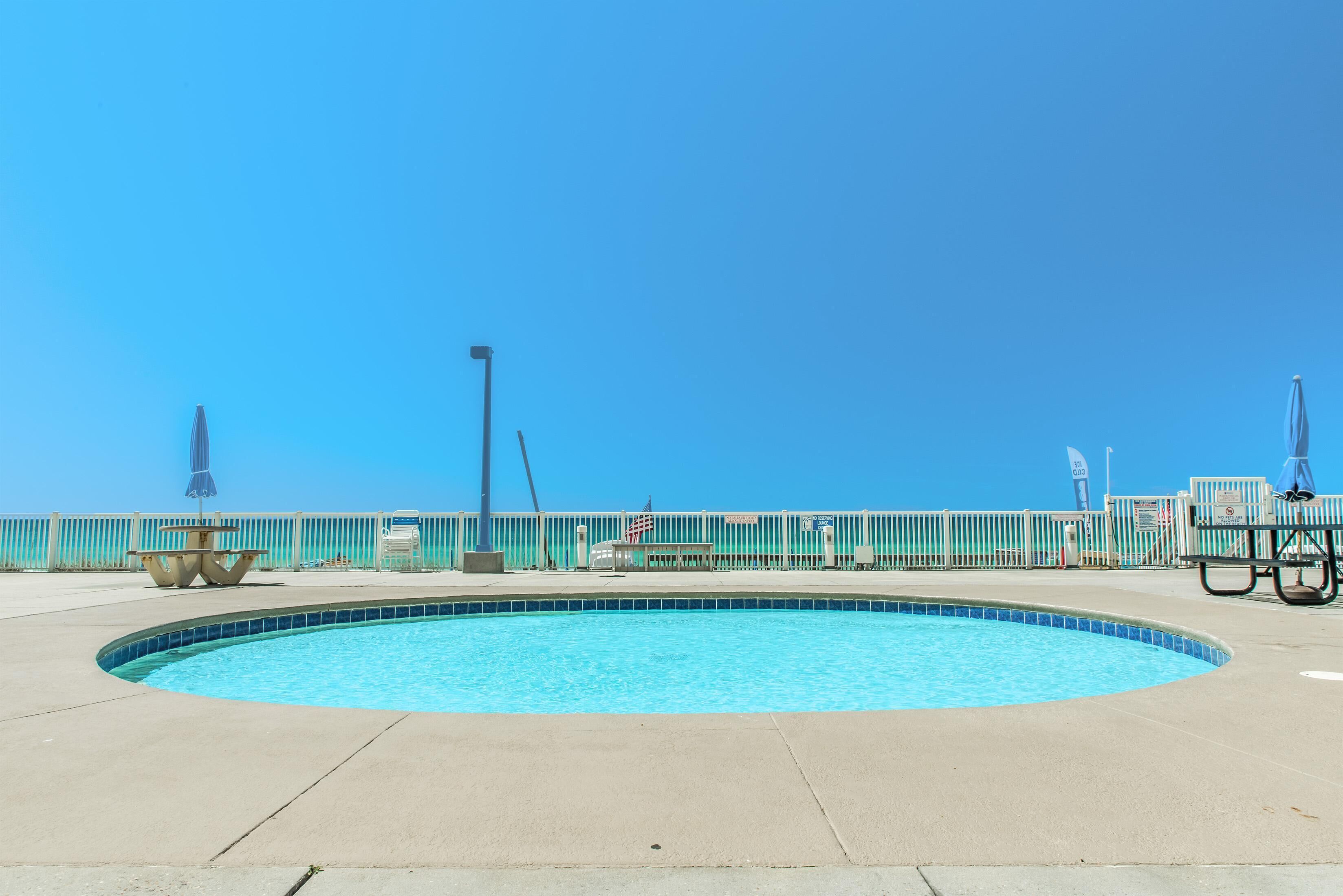 Un ciel d’un bleu éclatant, une piscine et une clôture ornée de drapeaux.
