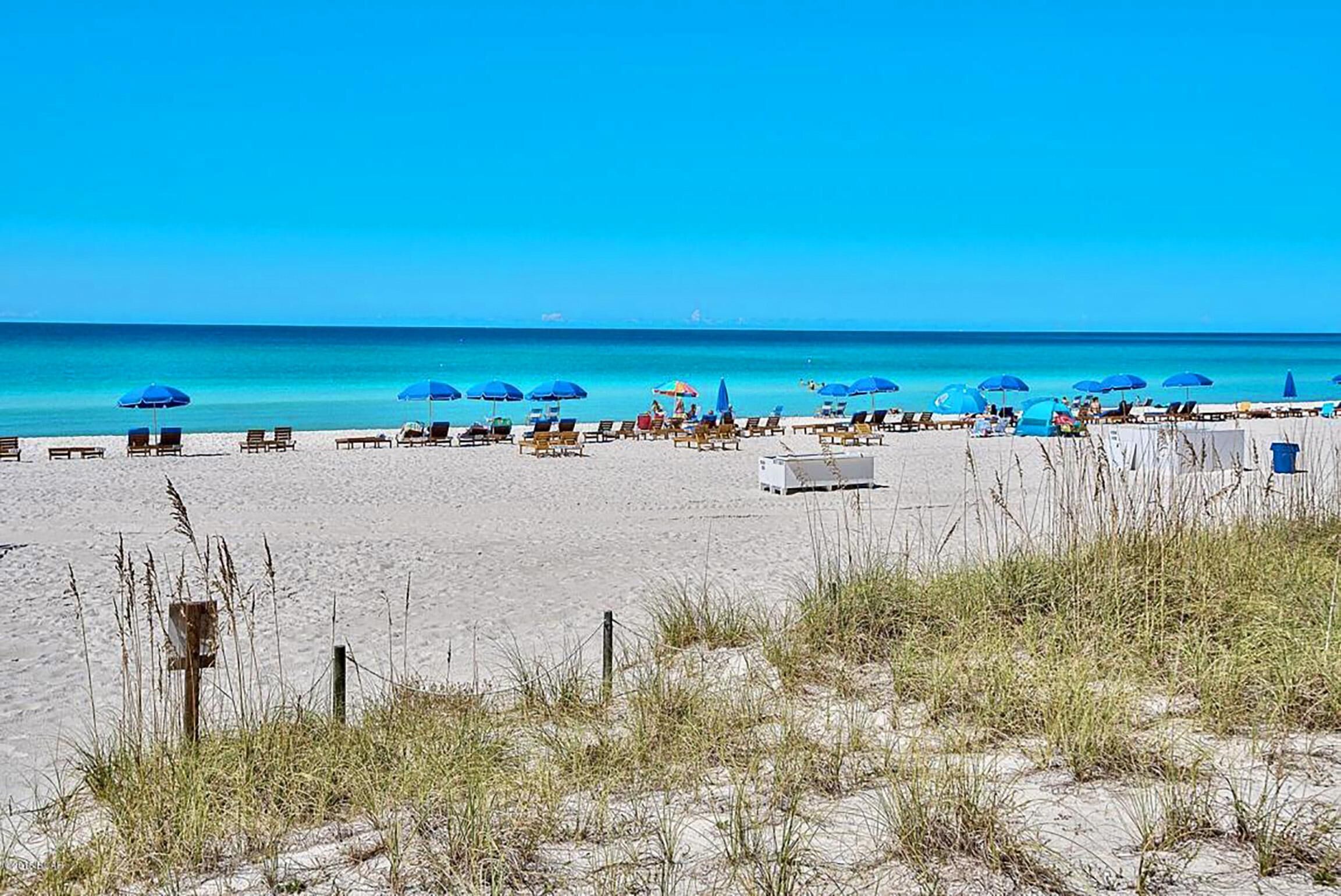 A beach with sun loungers and umbrellas, a clear sky, and the ocean in the background.