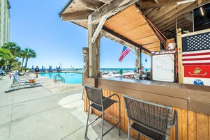 A wooden bar area with a poolside view, a flag, and a menu board.