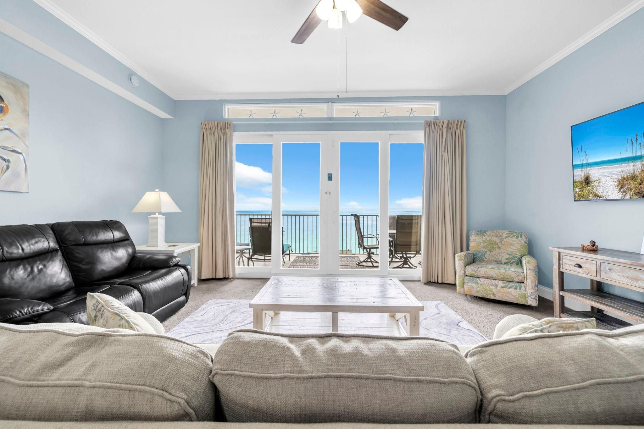 A living room with a black leather sofa, a white coffee table, and a view of the ocean through large glass doors.
