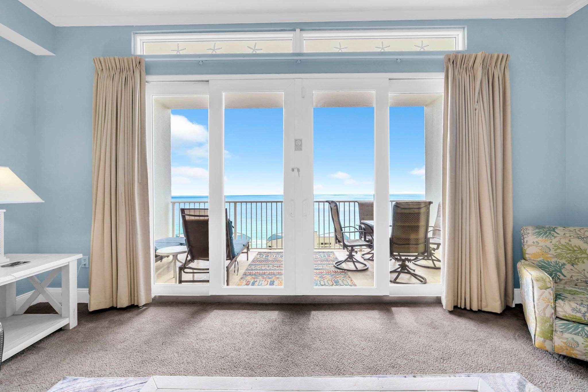 Une pièce dotée d’une porte-fenêtre coulissante donnant sur un balcon avec des chaises et une table, une console blanche et un fauteuil à motifs.