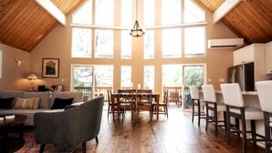 Un vaste espace de vie doté d’un haut plafond, d’un plancher en bois, d’une table à manger avec des chaises, d’un canapé et d’un coin cuisine avec des tabourets de bar.