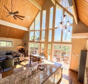 A spacious kitchen with a large island, wooden ceiling, and large windows.