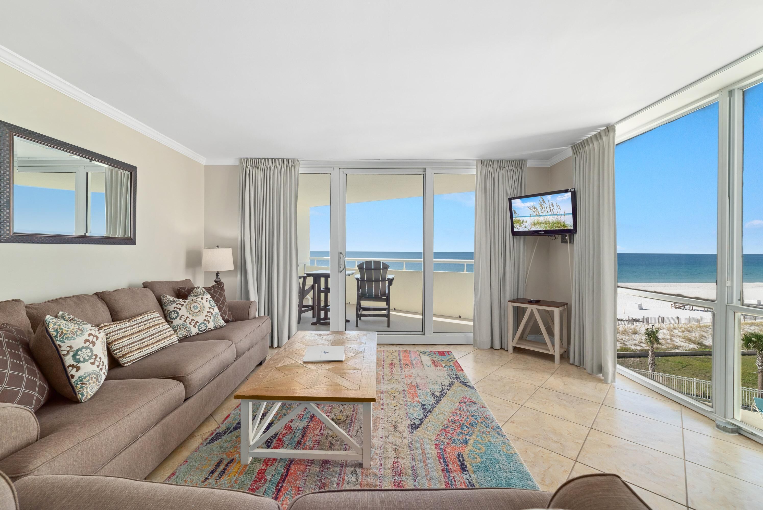 A modern living room with a sofa, coffee table, and TV, overlooking a beach.