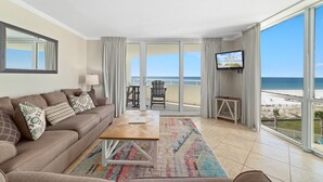 A modern living room with a sofa, coffee table, and TV, overlooking a beach. - Perdido Sun 406 (Pensacola)