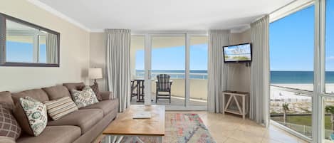 A modern living room with a sofa, coffee table, and TV, overlooking a beach.