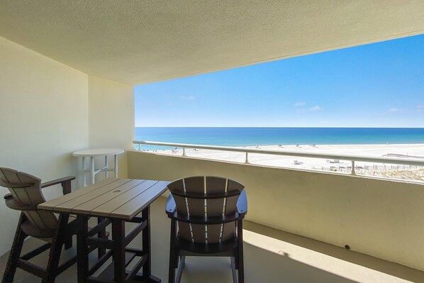 A balcony with a wooden table and two chairs, overlooking a beach with clear skies. - Perdido Sun 406 (Pensacola)
