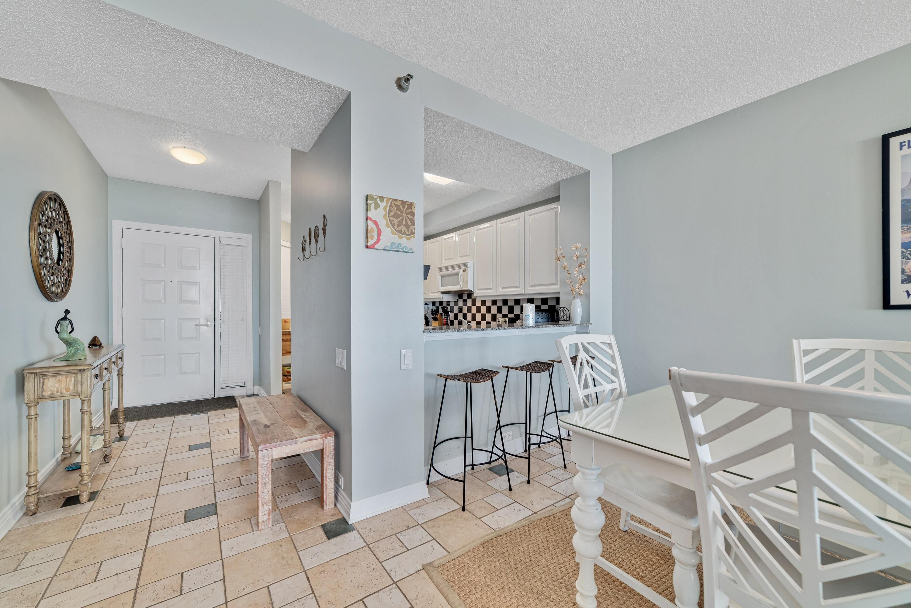 A modern kitchen with white cabinets, a dining area with a white table and chairs, and a small wooden bench.