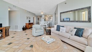 Een ruime woonkamer met een beige bank, een rond geweven bijzettafeltje en een plafondventilator.