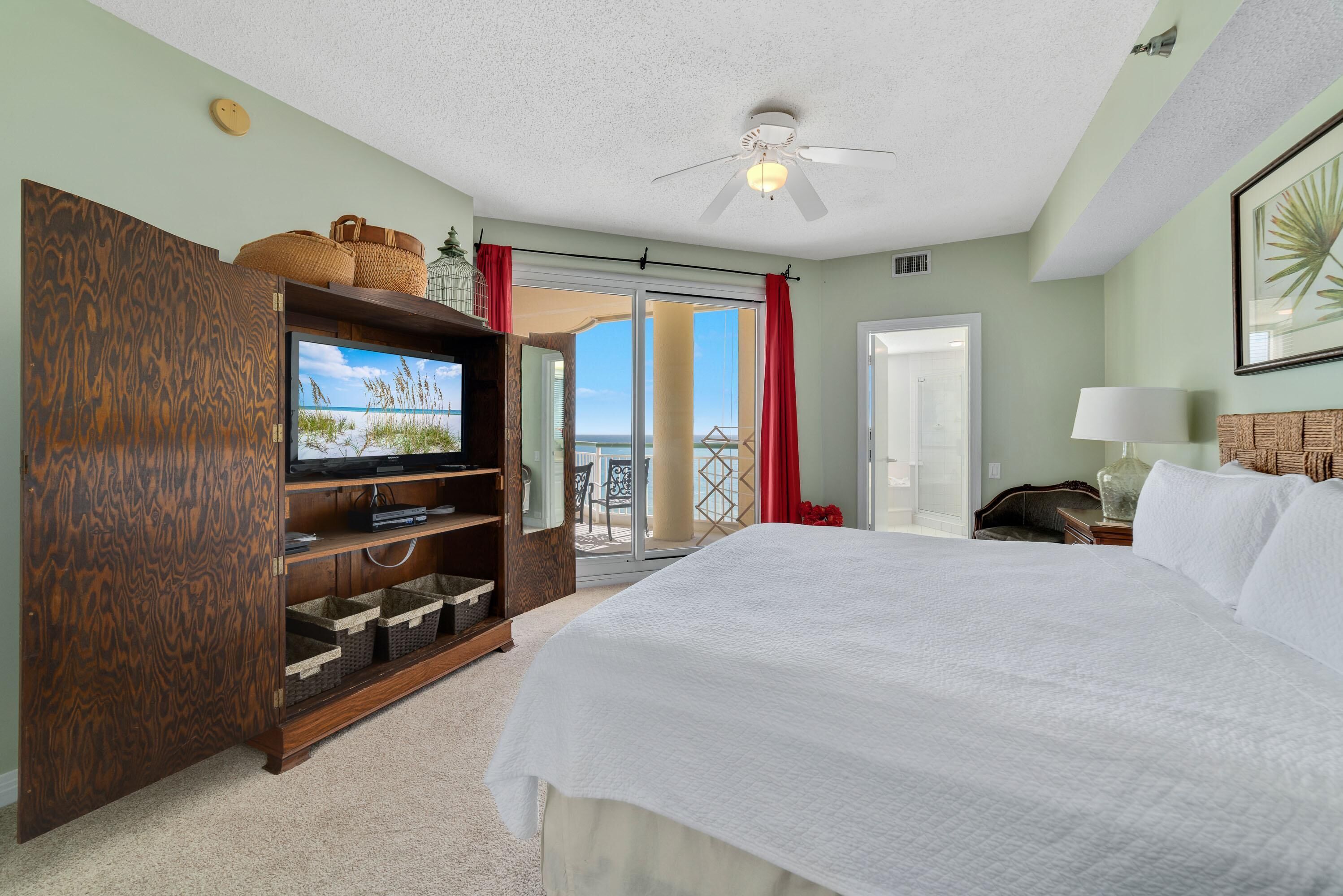 Une chambre d’hôtel avec un grand lit, un meuble de rangement en bois intégrant un téléviseur, un ventilateur de plafond et une vue sur l’extérieur.