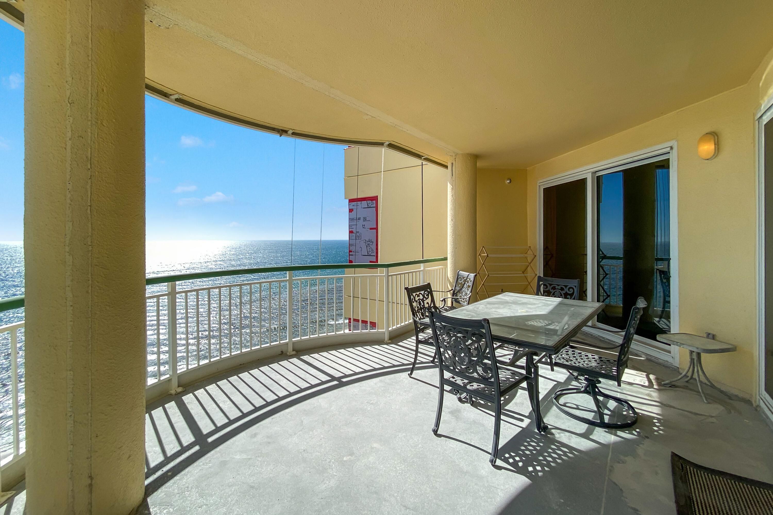 A balcony with a table and chairs, a view of the sea, and a door leading to an interior space.
