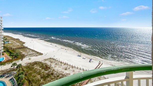 Uitzicht op het strand vanaf een balkon met een zwembad en strandstoelen.
