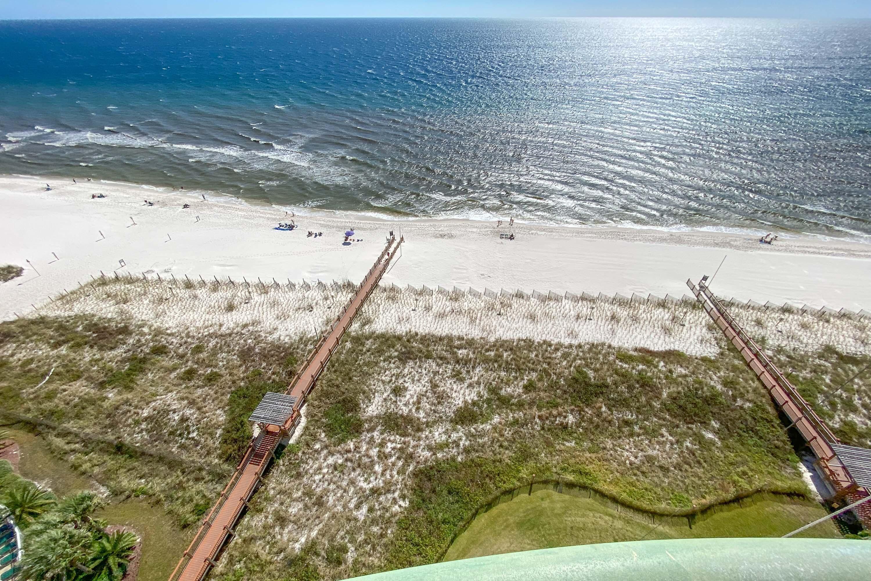A beach with a wooden pier extending into the ocean, sandy beach, and grassy dunes.