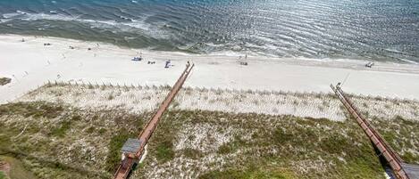 A beach with a wooden pier extending into the ocean, sandy beach, and grassy dunes.
