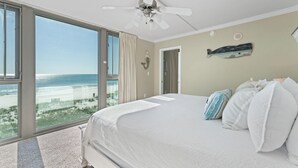 Een slaapkamer met een groot bed, een plafondventilator en uitzicht op zee.