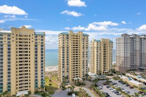 A high-rise hotel with multiple floors, a parking area, and a view of the beach. - Beach Colony Tower 5B (Pensacola)