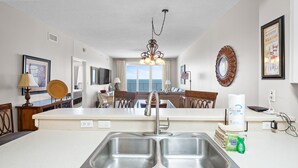 A modern kitchen with a central island, stainless steel sink, and a chandelier. - Windemere 807 (Pensacola)