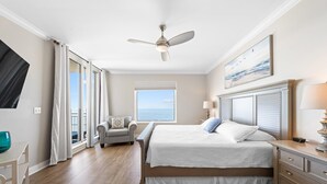 Ein Schlafzimmer mit einem großen Bett, einem Deckenventilator, Meerblick durch ein Fenster und einem Sessel am Fenster.