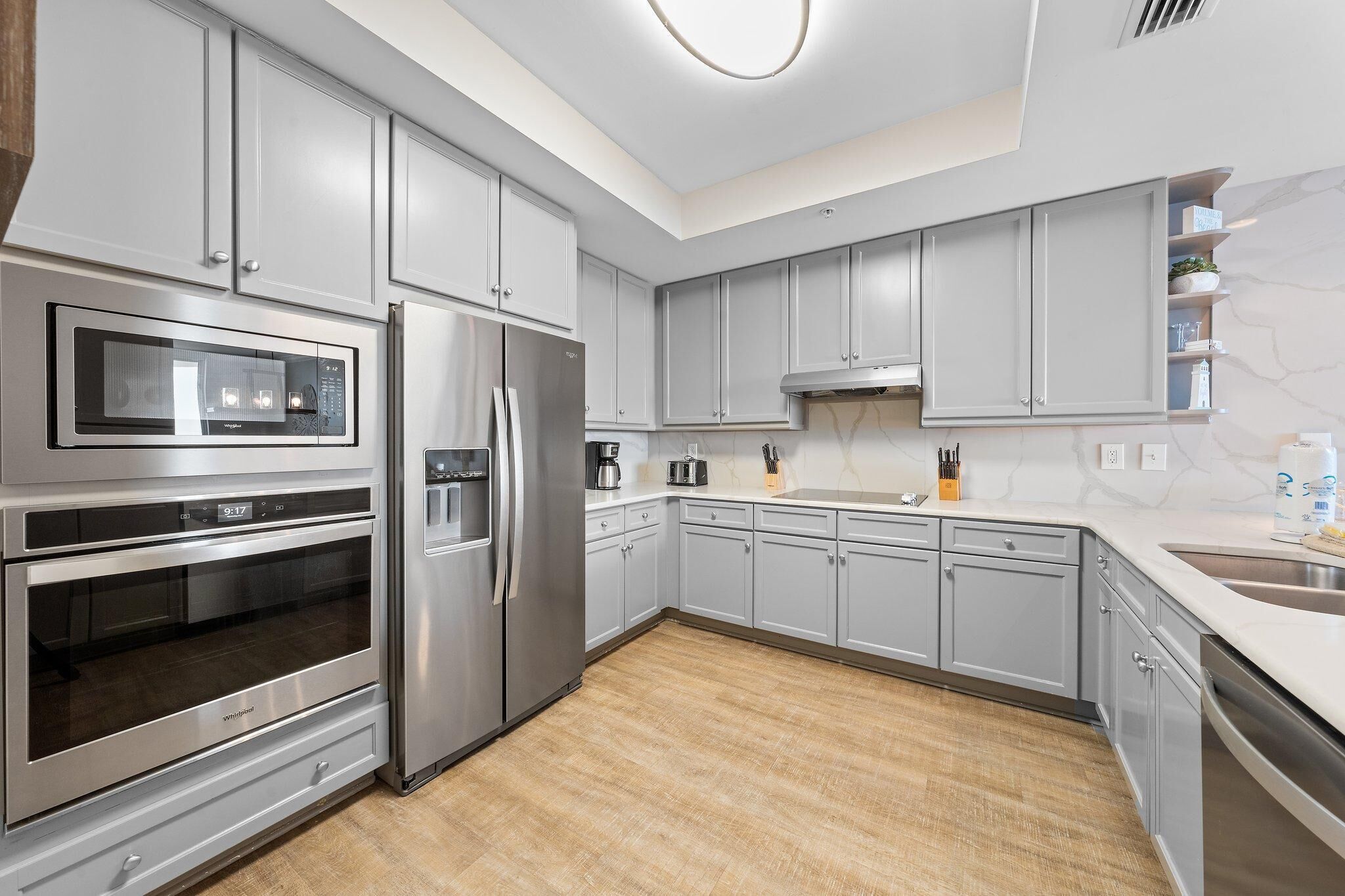 A modern kitchen with grey cabinets, stainless steel appliances, and a marble backsplash.