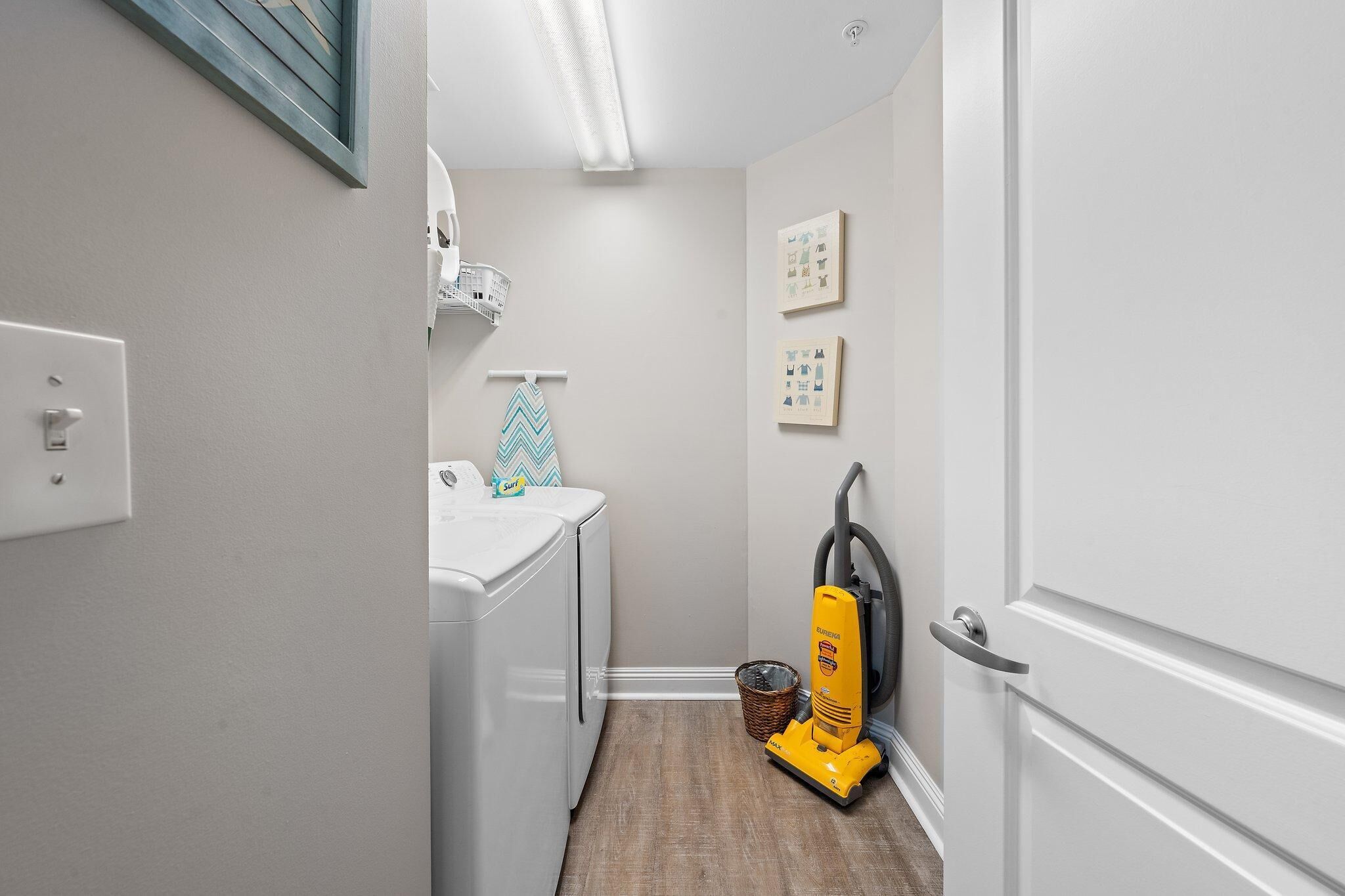 A laundry area with a washing machine, a drying rack, a vacuum cleaner, and a basket.