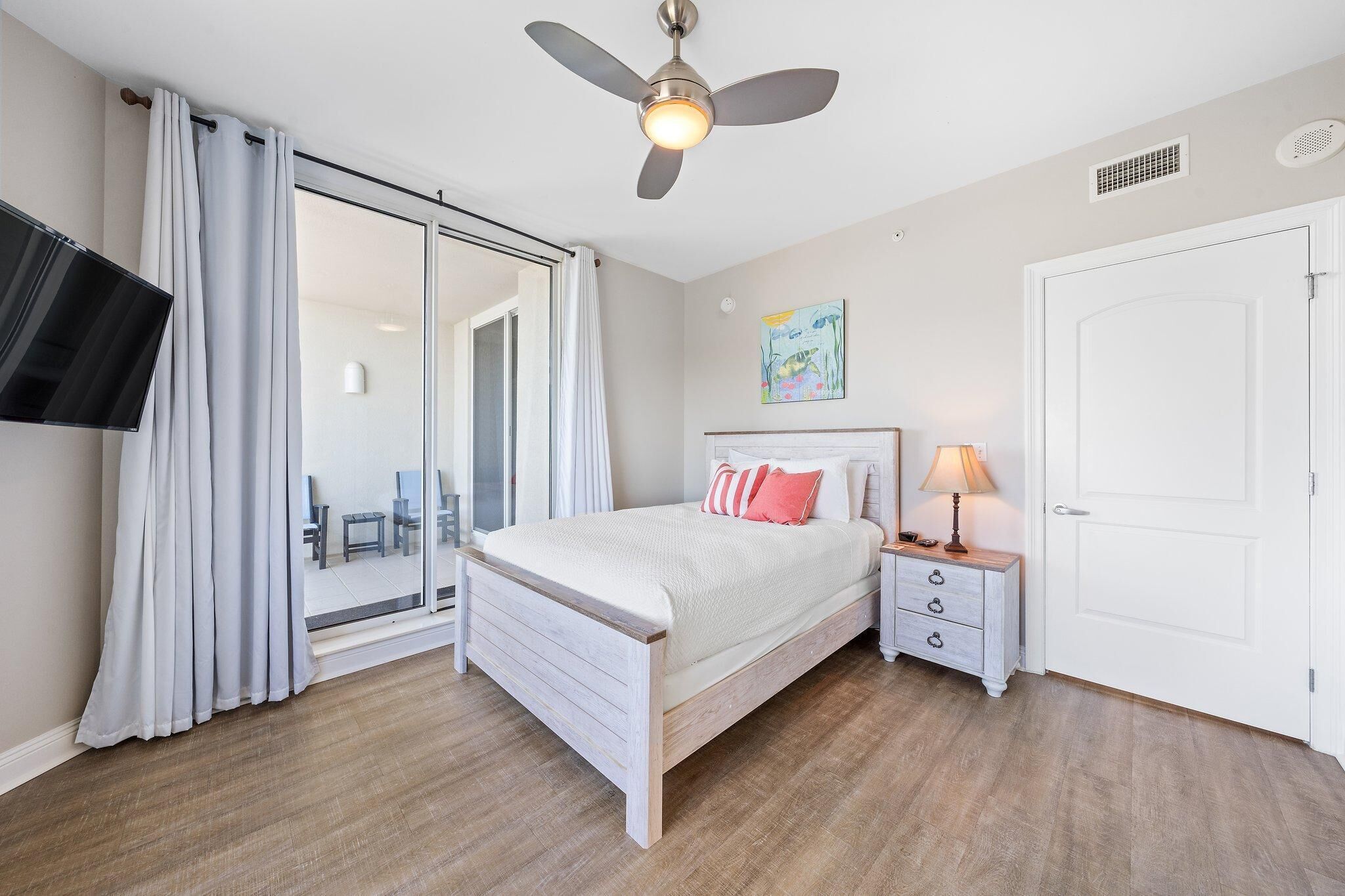 A bedroom with a bed, a nightstand, a ceiling fan, a sliding glass door, and a white door.