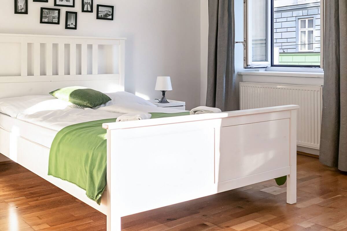 Un dormitorio ordenado con una cama blanca, un edredón verde y una ventana con cortinas.