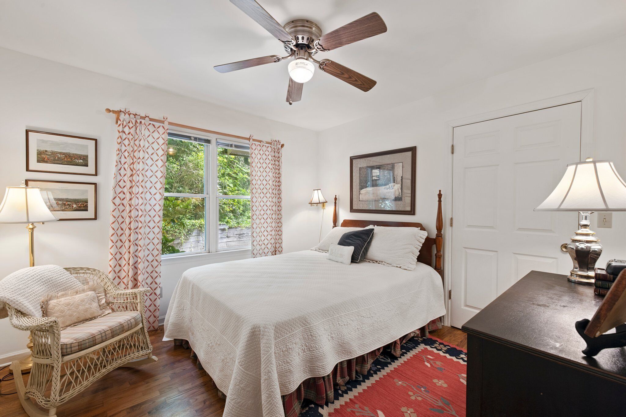A bedroom with a bed, a chair, a desk, a ceiling fan, and a window with curtains.