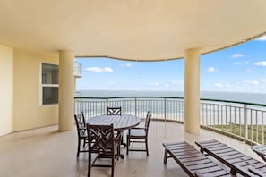 Enjoy the ocean view from this balcony with a round table, four chairs, and a bench.