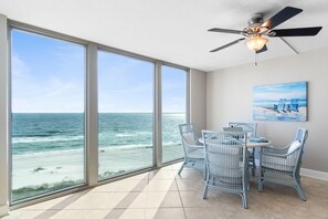 Una habitación con ventanas amplias que dan al océano, un ventilador de techo y una mesa con sillas.