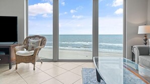 Una habitació amb una finestra gran amb vista al mar, una cadira de vimetla, un sofà i un televisor de pantalla plana.