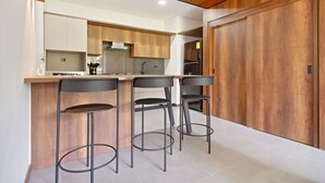 Eine moderne Küche mit Holzschränken, einer zentralen Kochinsel inklusive Barhocker und einer großen Holztür.