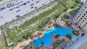 An aerial view of a resort with a beach, multiple pools, and a hotel building.