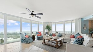 A spacious living room with a large window, a ceiling fan, and a view of the city. - Caribe C1010 (Orange Beach)