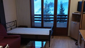 Ein Zimmer mit einem Bett, einem Glastisch, einem roten Sofa, einem Holzboden und Blick auf eine verschneite Landschaft durch eine Schiebetür.