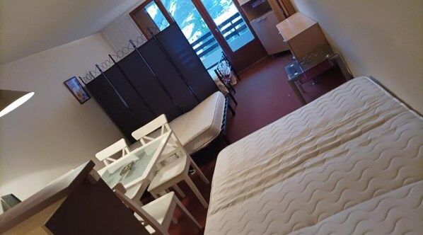 A hotel room with a bed, a desk, a chair, a wardrobe, and a window with a view of the outside.