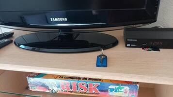 Un écran Samsung, une horloge numérique et un jeu de société Parker sur une surface en bois.