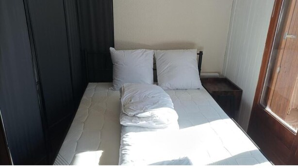 Ein ordentlich bezogenes Bett mit weißen Leinen und Kissen, ein Nachttisch aus Holz und ein Fenster mit Vorhängen.